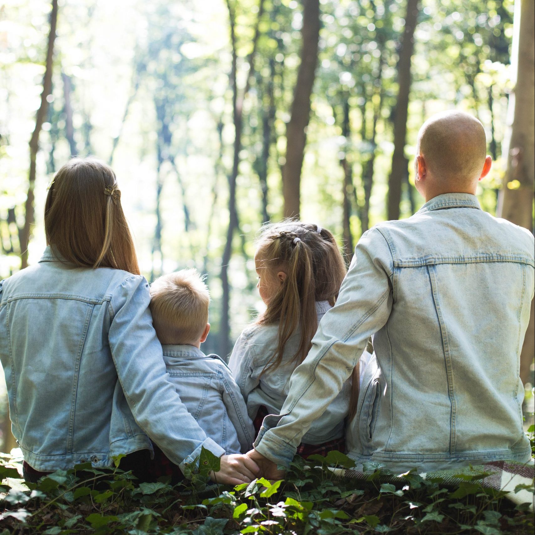 man and woman holding hands together with boy and girl looking at green trees during day